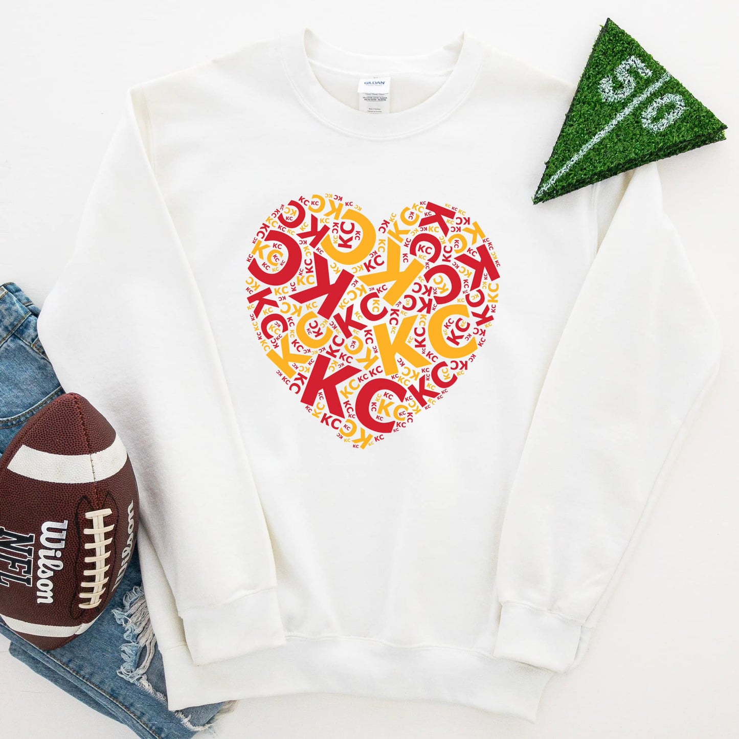 Photo is a mock up of the design. Design is red and gold in color and pressed on a white sweatshirt. Design says KC multiple times in the shape of a heart.