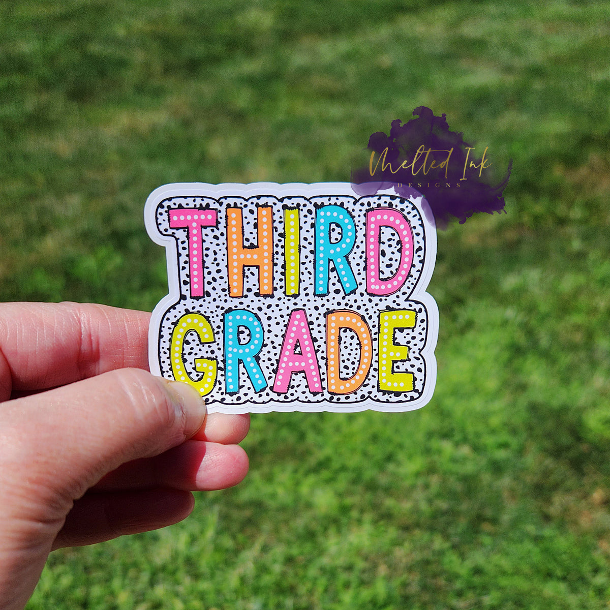 Photo is of a sticker that says third grade and has a black polka dot outline around it.