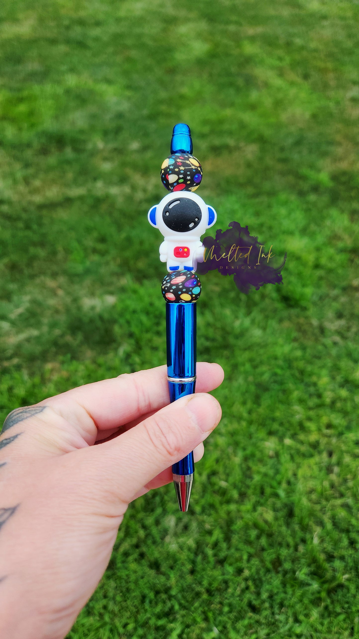 Photo is a metallic blue beaded ink pen that consists of an astronaut focal bead and includes 2 solar system silicone beads. Ink is black.
