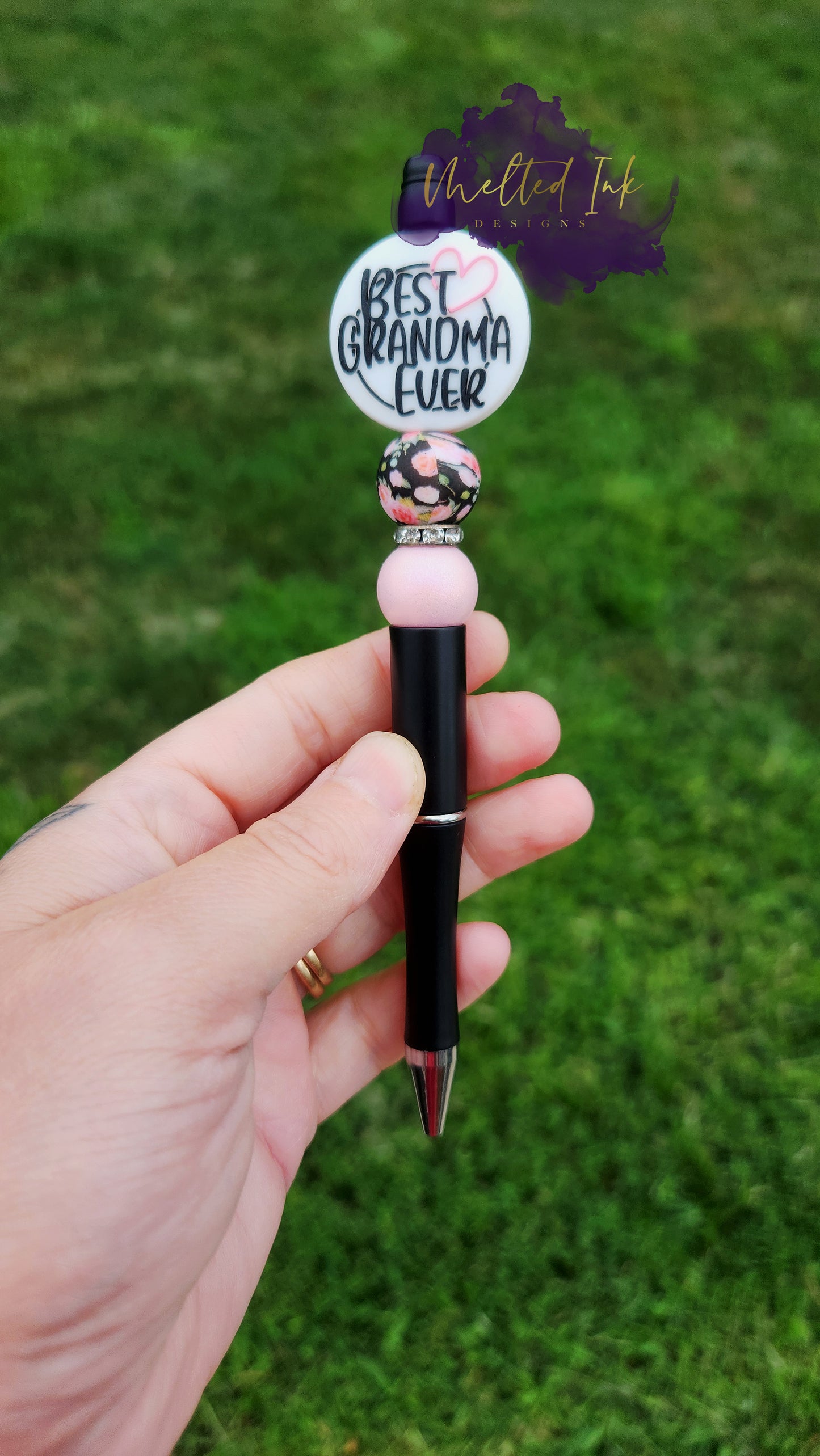 Photo is beaded black ink pen that showcases a round focal bead that says best grandma ever. Accenting the focal bead is a pink floral printed and a light pink silicone bead. A rhinestone spacer has been added to add a bit of sparkle. Ink is black.