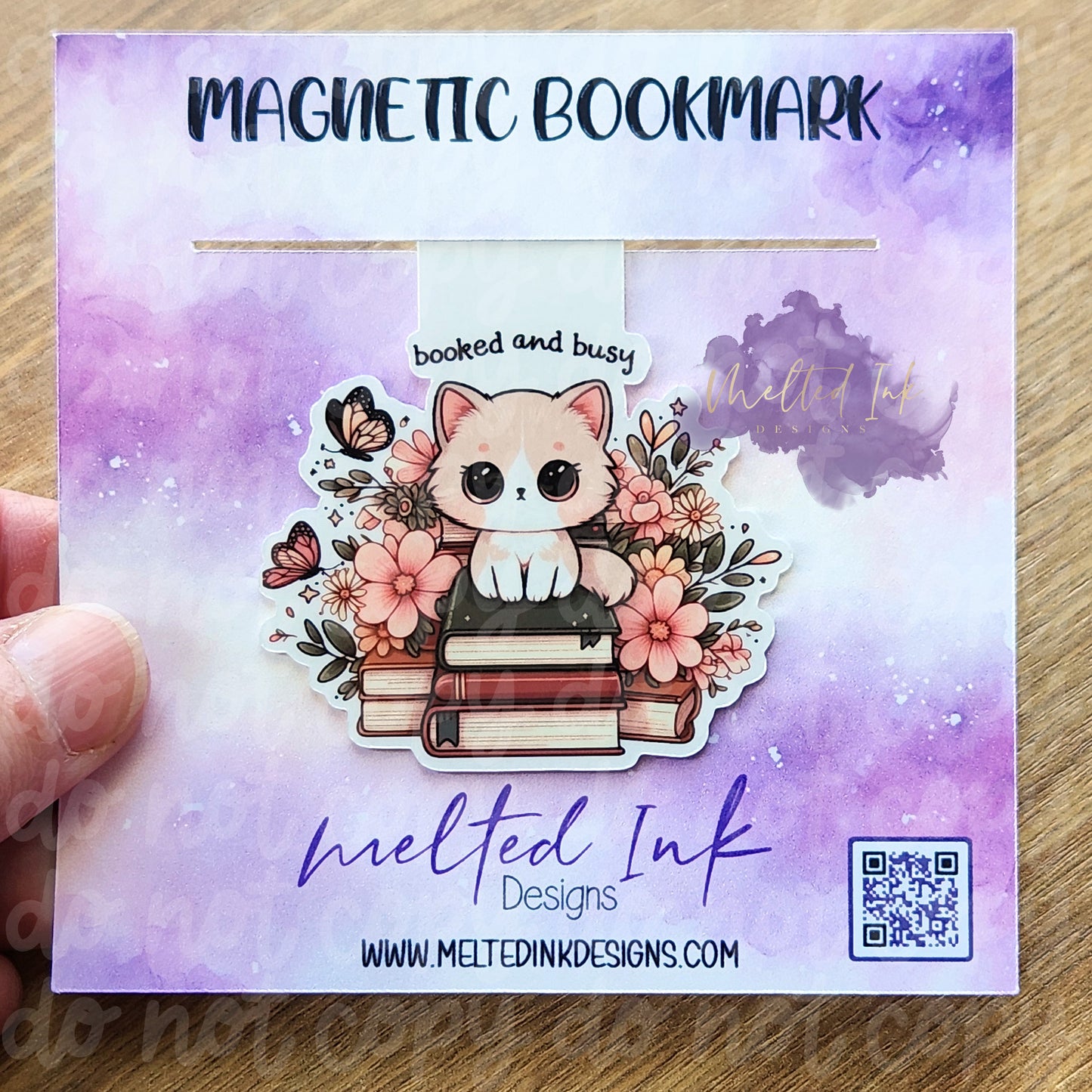 This magnetic bookmark showcases the phrase "Books and Busy," featuring an adorable cat perched atop a stack of books. The background is adorned with colorful flowers and butterflies, adding a whimsical touch to the scene.