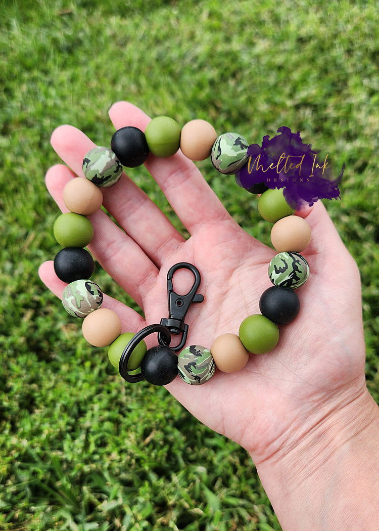 Photo consists of a keychain wristlet that has alternating camoflauge, black, tan and military green silicone beads. Includes a black keyring.