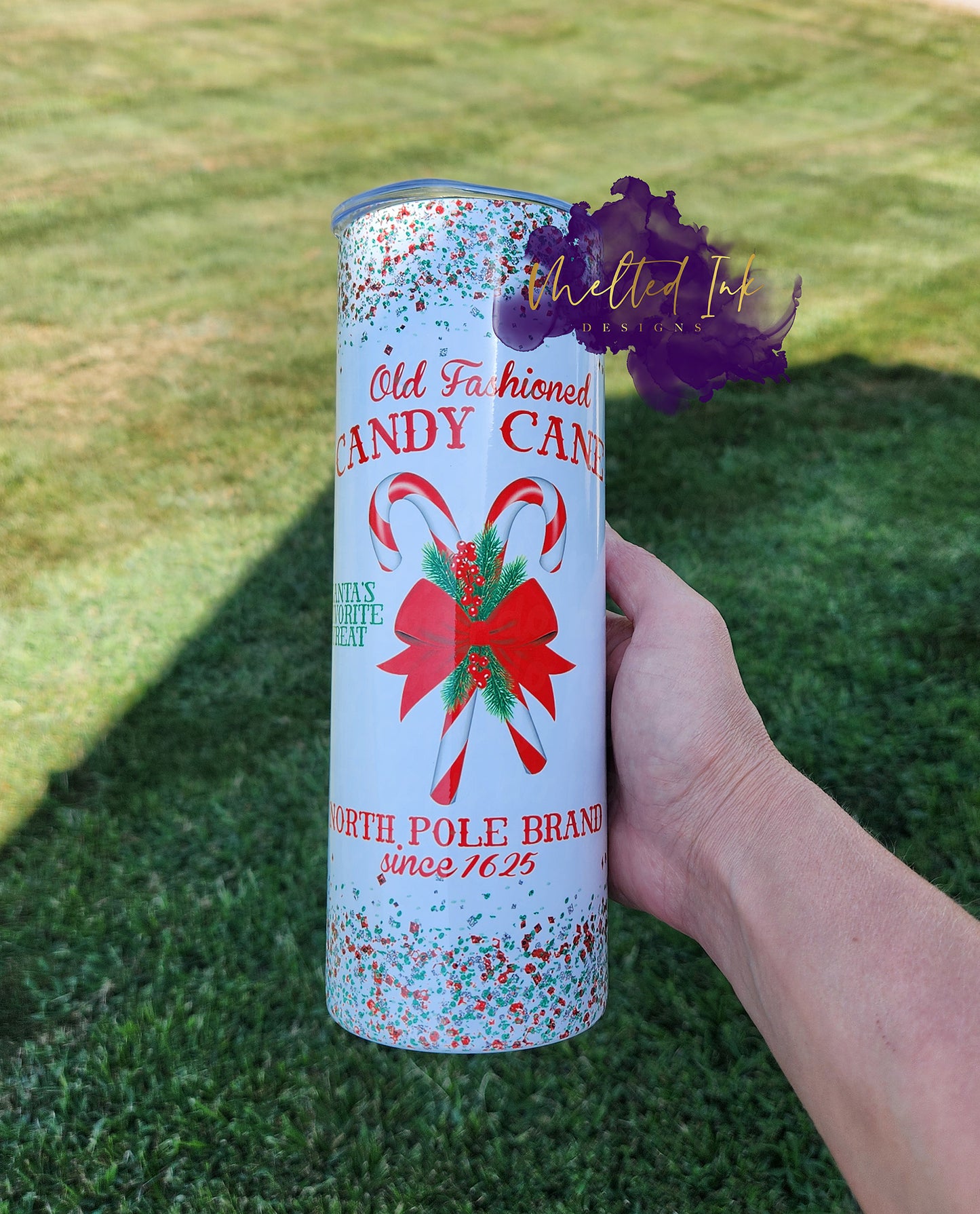 Photo is features a 20oz tumbler with faux red and green glitter. Tumbler says old fashioned candy cane north pole brand since 1625 and has 2 candy canes with a bow on top of them.