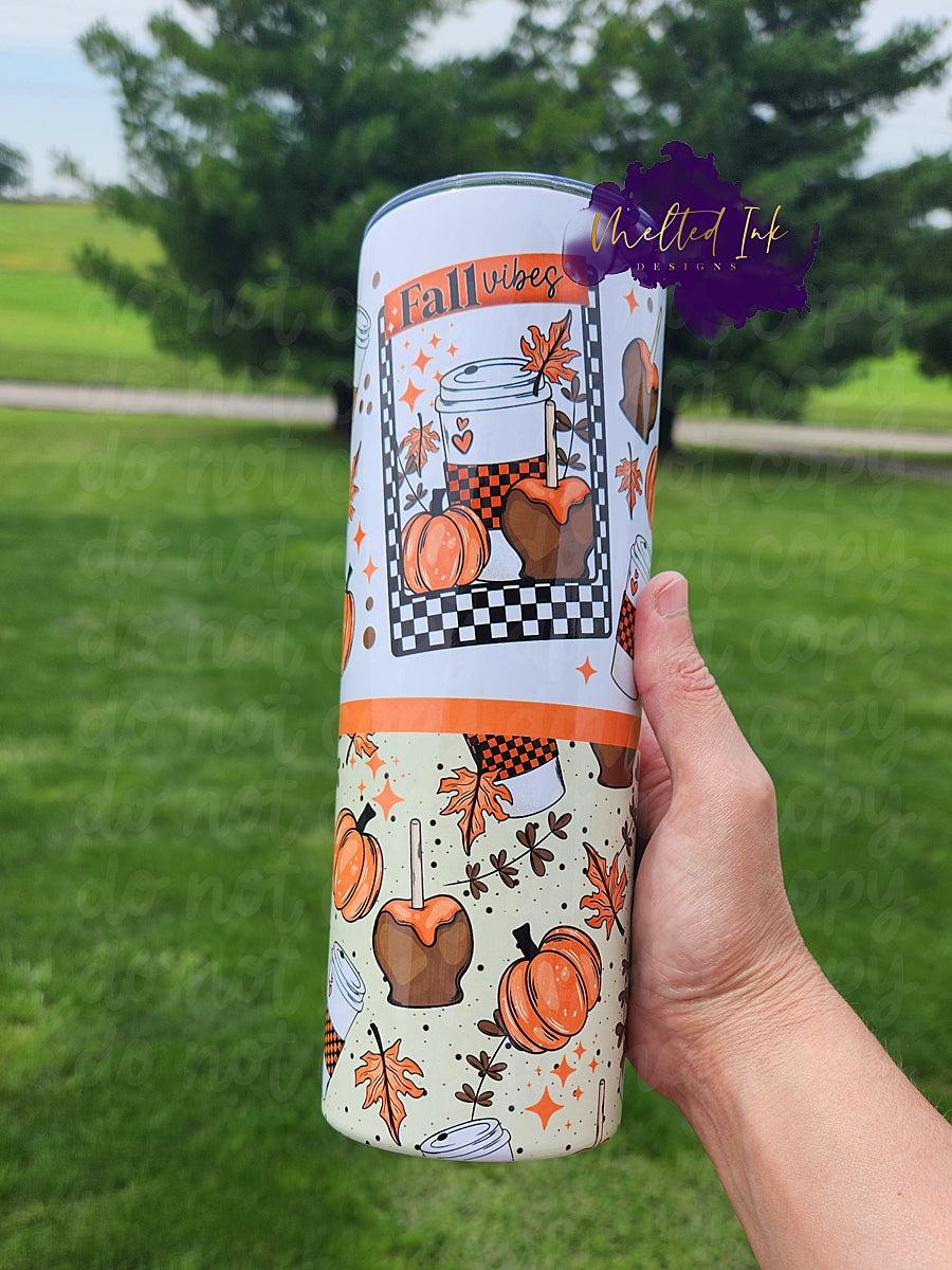 The photo features a 20oz fall tumbler that embodies the cozy spirit of the season. It prominently displays the phrase "Fall Vibes" within a stylish black and white checkered frame. Surrounding the frame are delightful autumn elements, including a pumpkin, a caramel apple, and a coffee drink, all of which capture the essence of fall.
