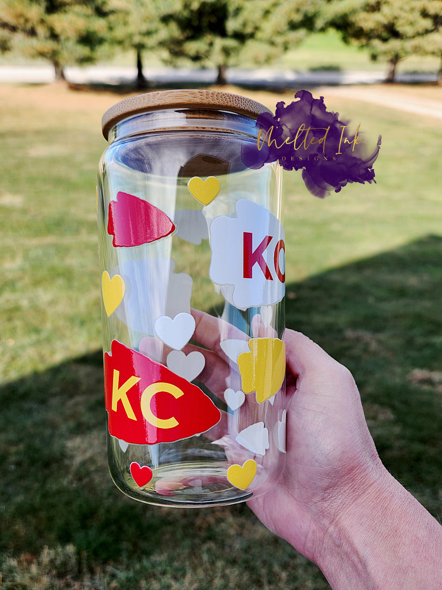 Picture is of a clear glass can with chiefs arrowheads and hearts in chiefs colors.