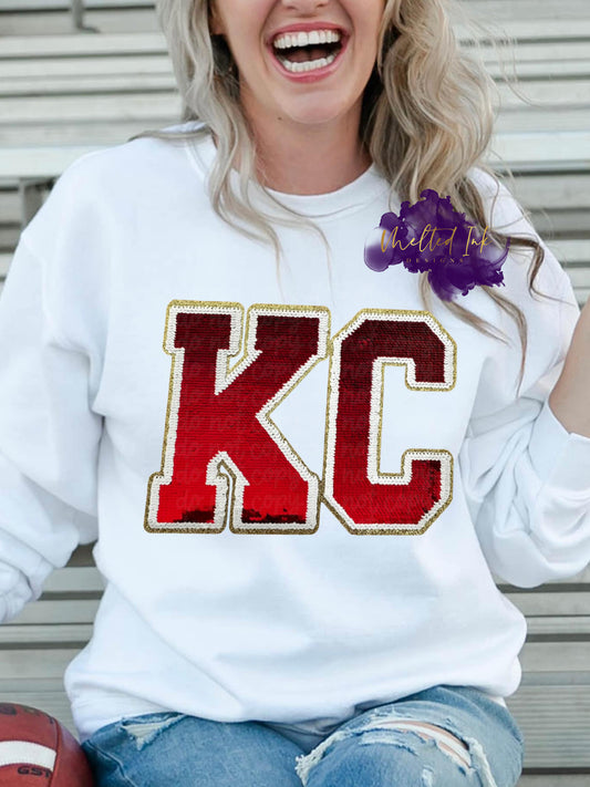 Photo is a mock up of design on a white sweatshirt. Design is of the letters KC with red sequins outlined with white sequins with a trim of gold.