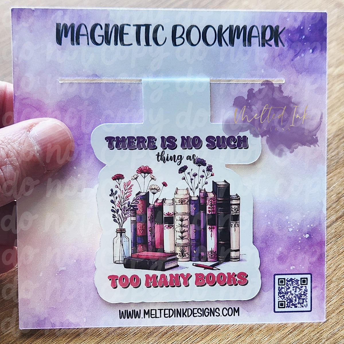 Photo is of a magnetic bookmark. It says there is no such thing as too many books. It has a picture of several books lined up side by side with little flowers.