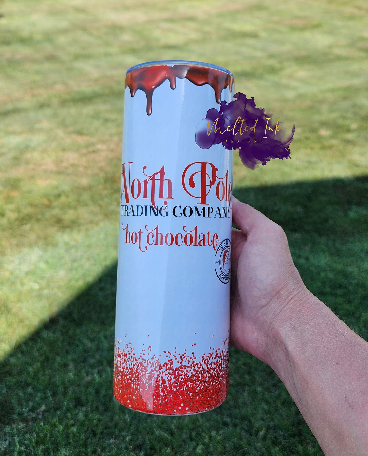 Photo consists of a 20oz tumbler that has melting chocolate at the top and faux red glitter at the bottom. Tumbler says North Pole trading company hot chocolate.