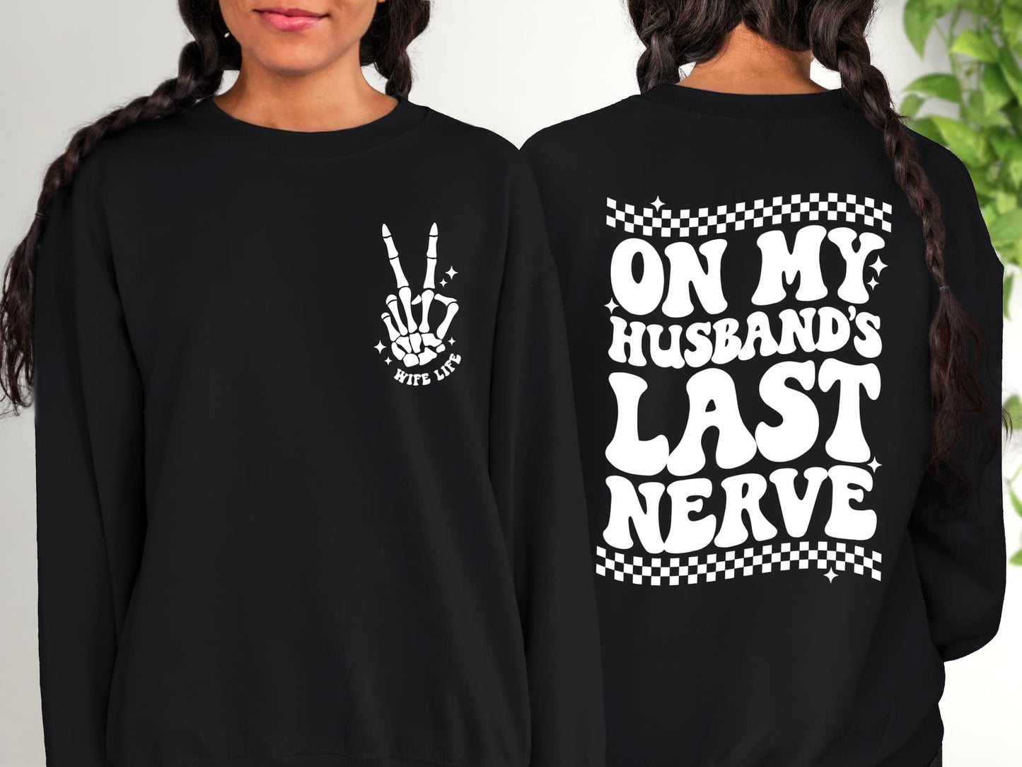 Picture shows design pressed on black crewneck as pocket design option. The front pocket design has a picture of a skeleton hand holding peace sign up with two fingers. Under it the design says wife life.