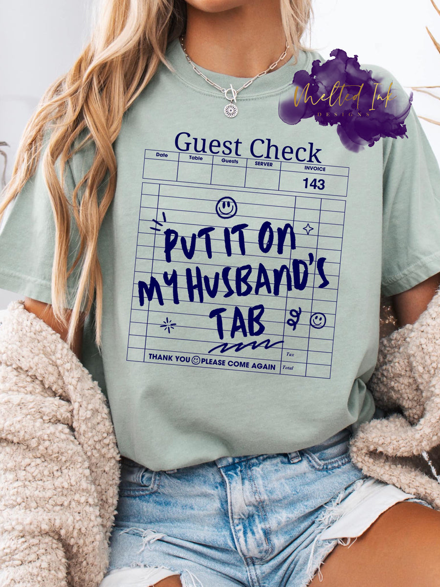 Funny "Put It On My Husband's Tab" women's t-shirt – humorous graphic tee for wives, casual gift idea, playful fashion statement for girls' night out or bachelorette party.