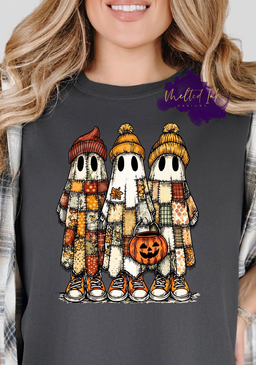 Image shows three cartoon-style ghosts wearing patchwork quilted robes, fall beanies, and sneakers. One ghost holds a pumpkin candy bucket. The design features warm autumn tones of orange, mustard, green, and cream — blending cozy fall and Halloween themes.