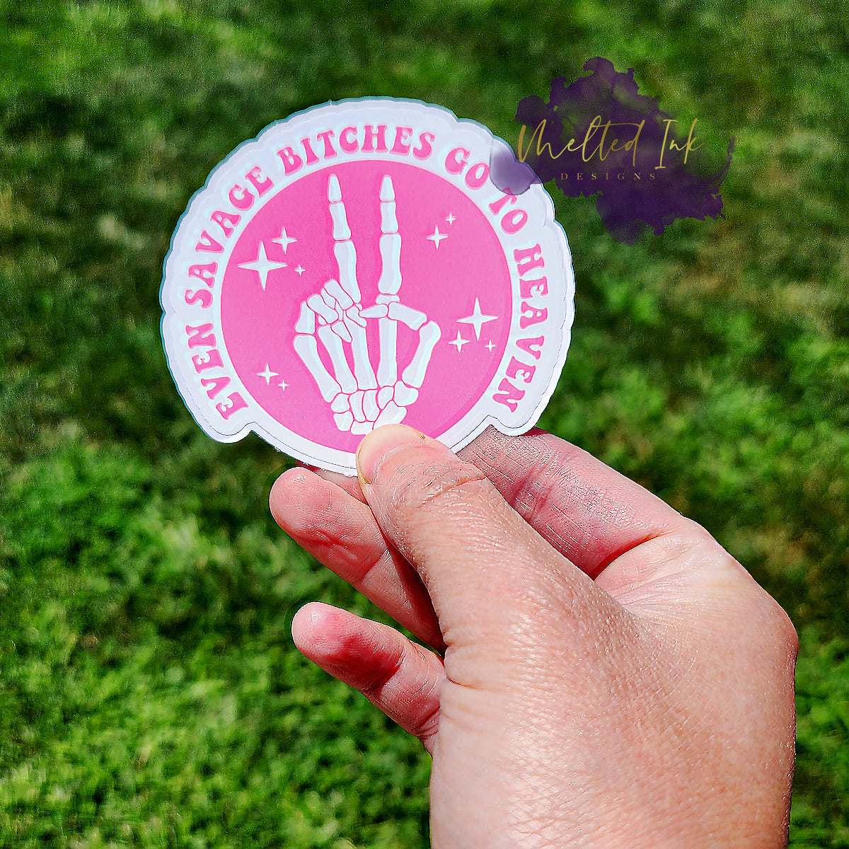 Photo is of a sticker that says Even Savage Bitches go to heaven and has a picture of a skeleton hand giving the peace sign. Ink is pink.