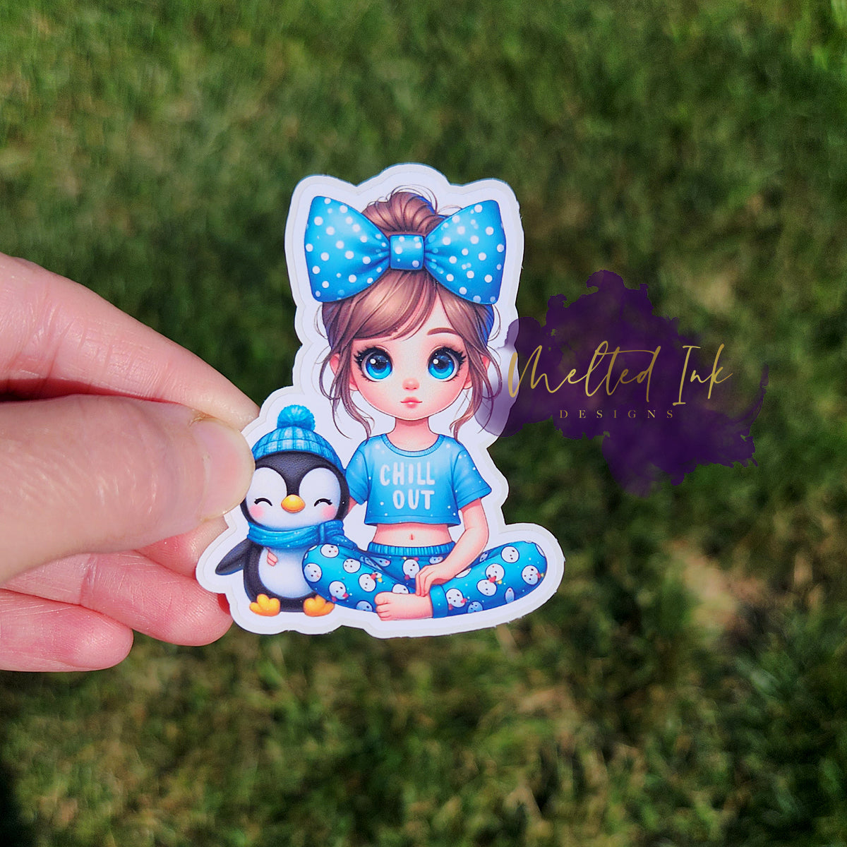 Photo is of a sticker that has a little girl with a bow in her hair, snowman pants and a shirt that says chill out. Next to her is a little penguin in a pom pom hat and scarf.