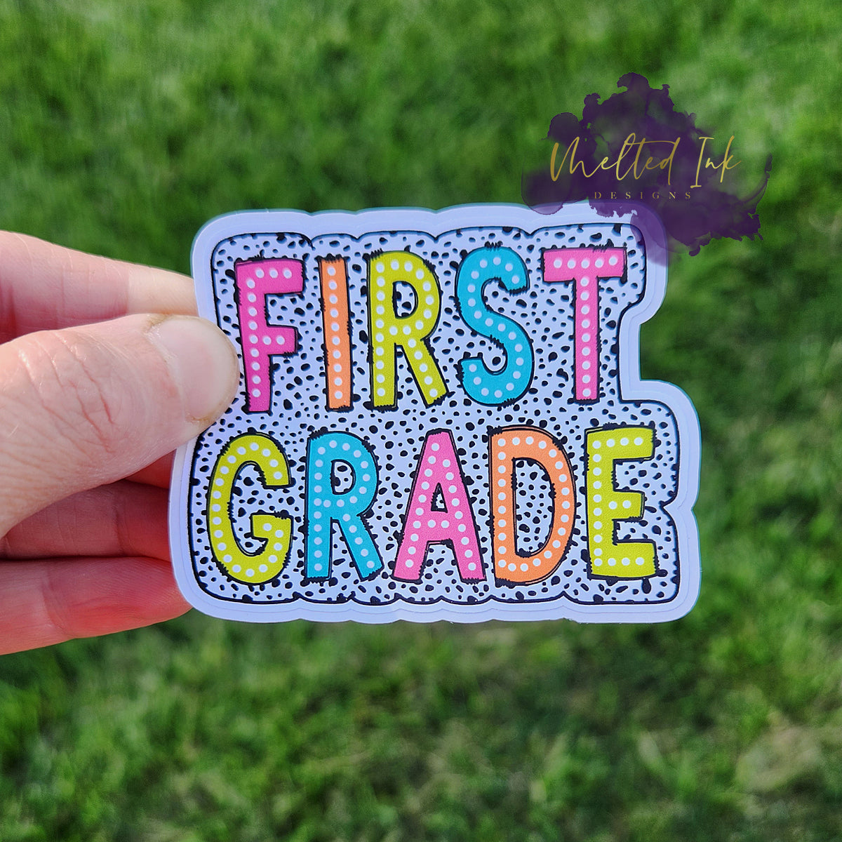 Photo is of a sticker that says first grade and has a black polka dot outline around it.