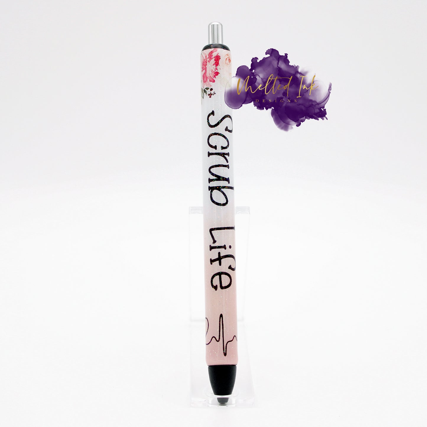 Photo consists of an epoxy pen that has a pen wrap that says scrub life. It has a floral design at the time with a heartbeat wrapped around the bottom part. Has a glitter overlay and comes with black ink.