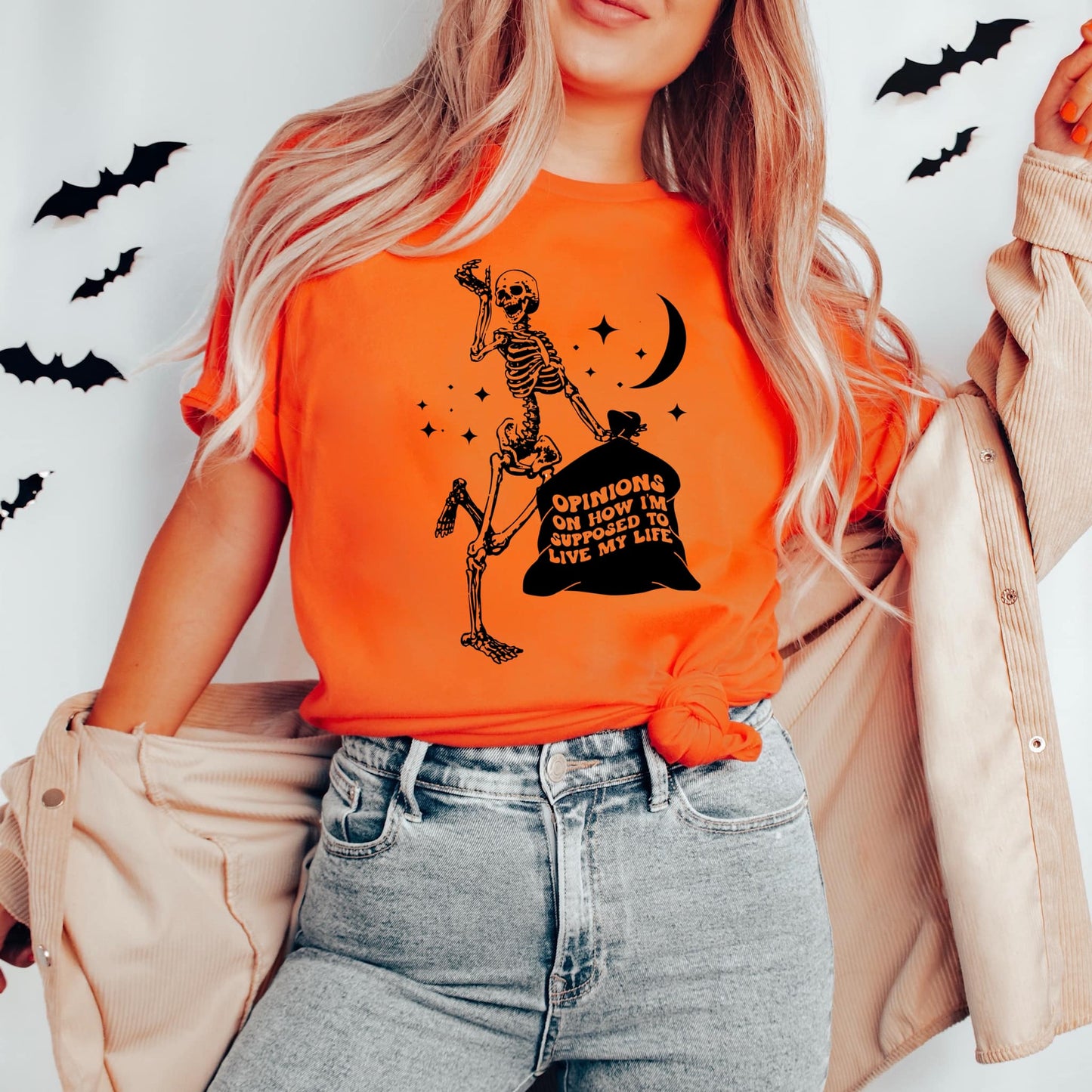 Photo is a mock up of the design. Design is black in color and is pressed on an orange shirt. Design is of a skeleton holding a trash bag. The words on the trash bag read opinions on how I'm supposed to live my life.