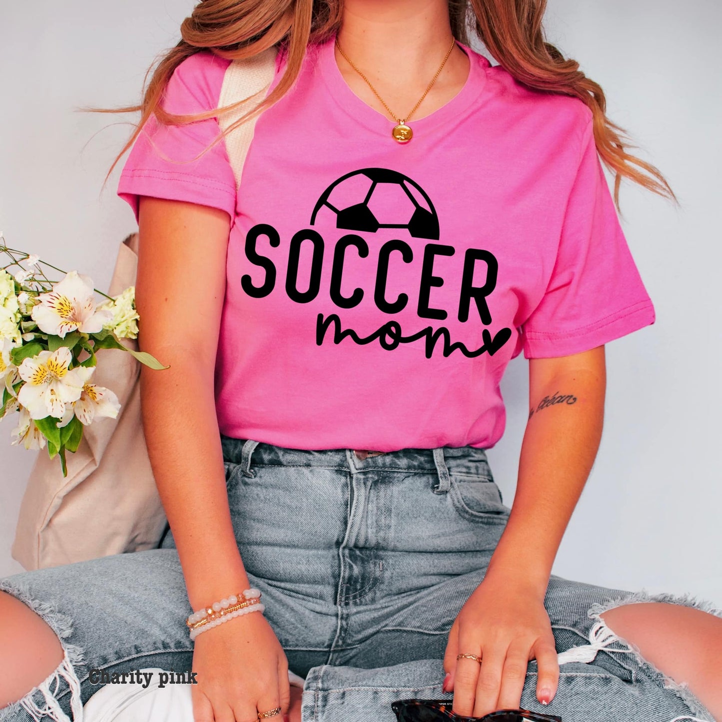 Photo is a mock up of the design. Design print is black and pressed on a pink shirt. Design says soccer mom with half picture of a soccer ball above the word soccer.