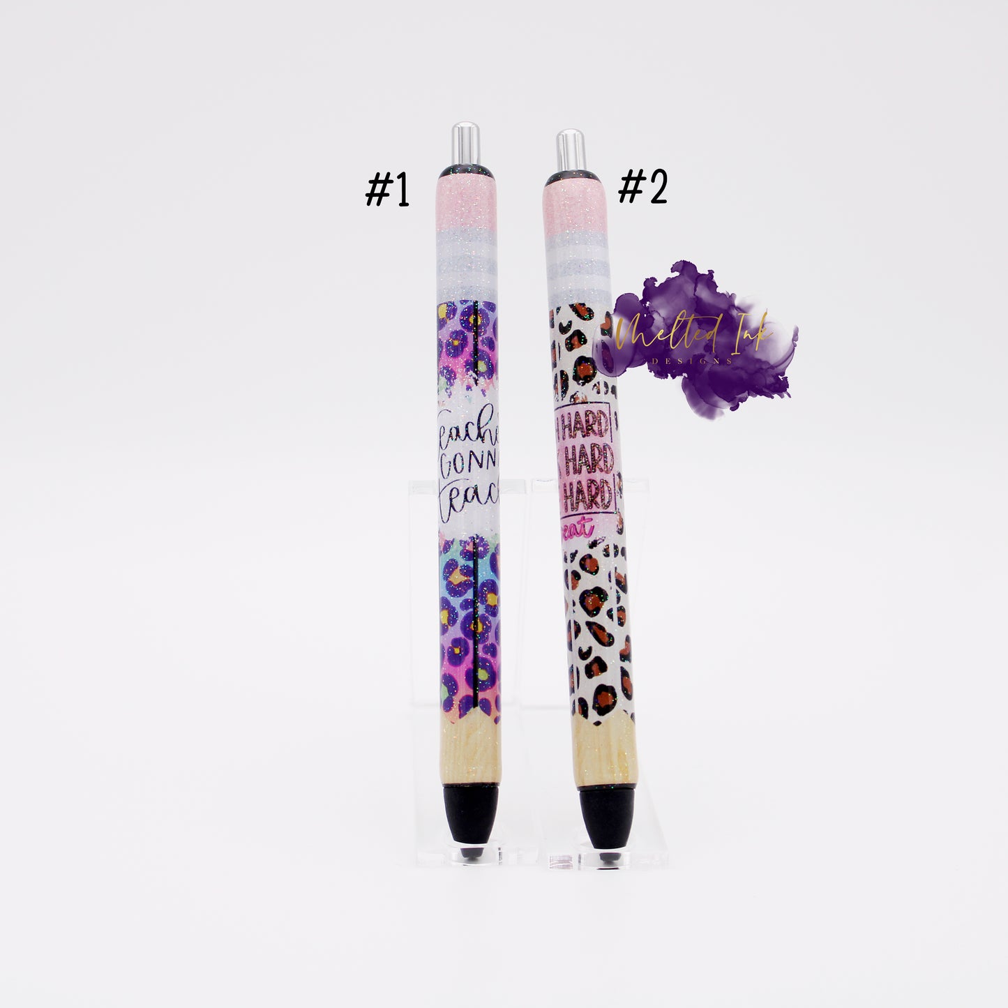 Photo consists of 2 different epoxy pens. #1 is a pencil wrap style pen that has colorful leopard print that says teacher gonna teach. #2 is pencil style wrap that is leopard print and says work hard, play hard, teach hard. Both pens have glitter overlay and have black ink.