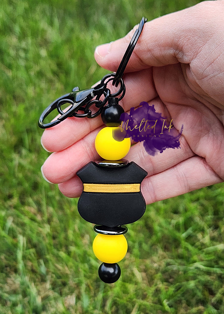 Photo consists of a beadable keychain bar that has a thin yellow line badge with solid yellow accenting silicone beads.