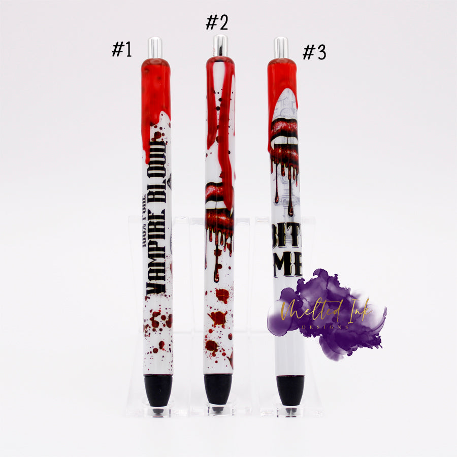 Photo consists of 3 different epoxy vinyl wrapped pens. #1 says 100% vampire blood with blood splatters. #2 has vampire lips with blood splatters and #3 has vampire lips/teeth that says bite me. All there have fake dripping blood and come with black ink.
