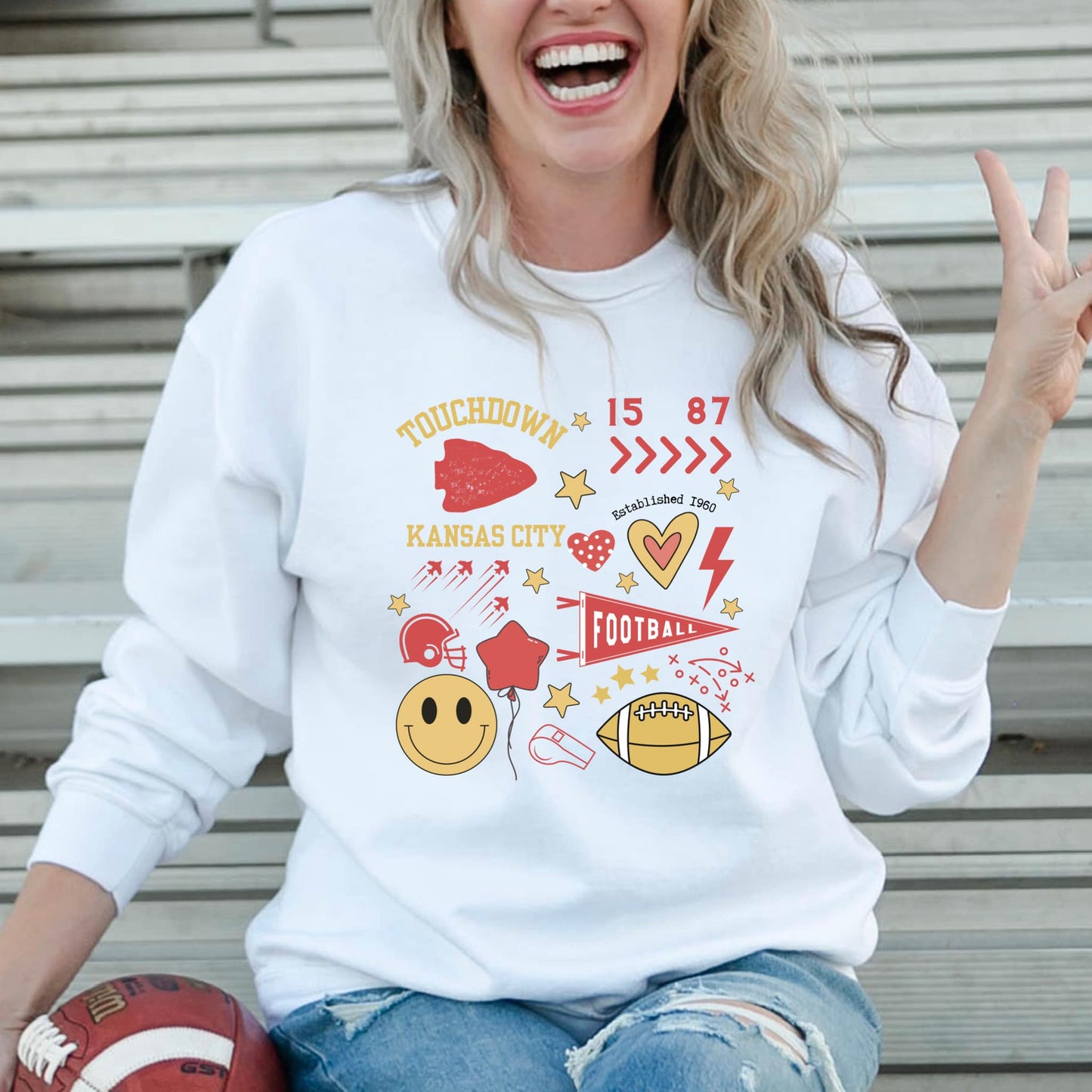 The product photo provided is only a mock up of the design. Design print is gold and red for Chiefs colors. Design has multiple pictures on it such as a red arrowhead, red helmet, red star balloon, gold smiley face, gold football, red football banner, hearts, red thunderbolt and the numbers 15 and 87. It also says Touchdown Kansas City and includes several gold stars. 