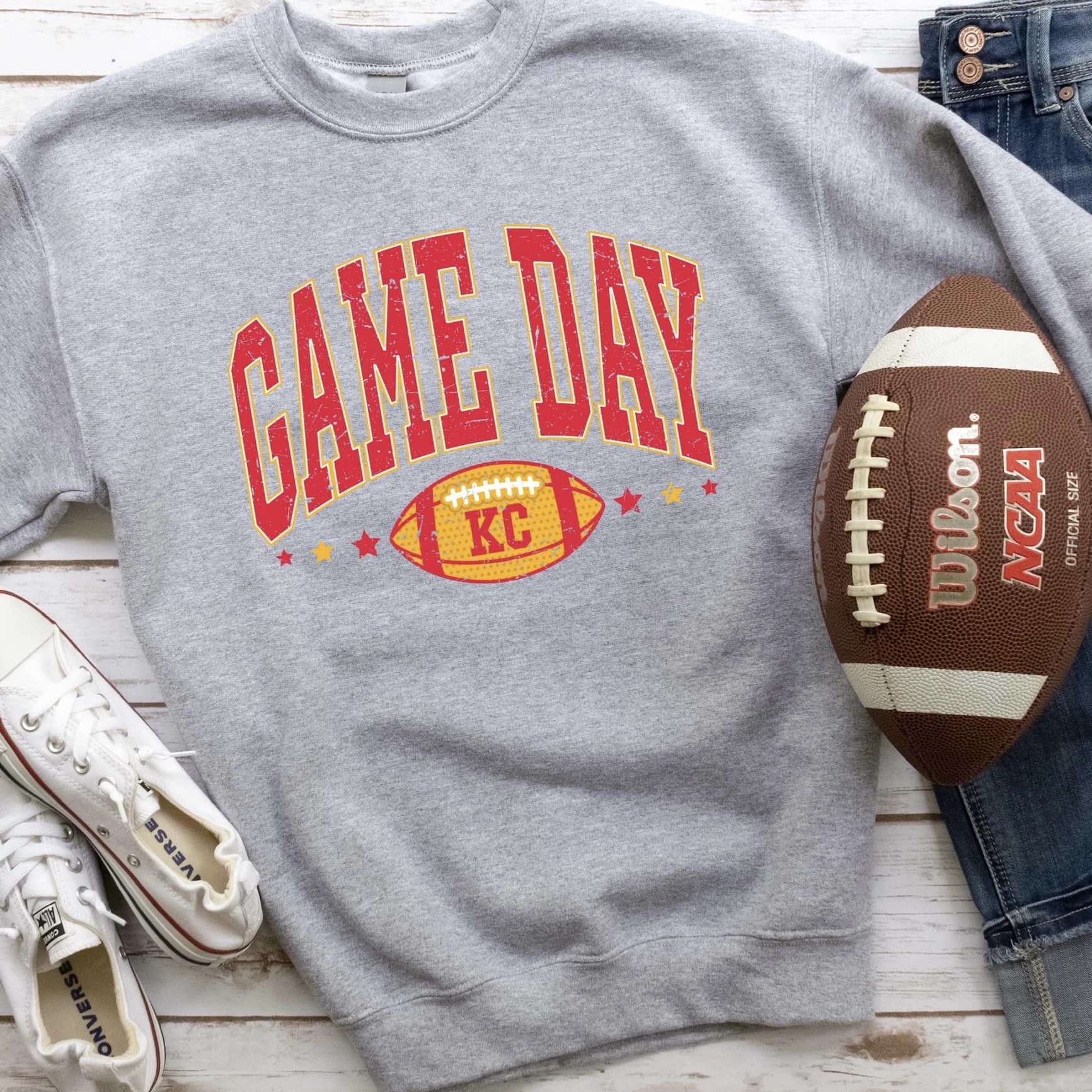 The product photo provided is only a mock up of the design. The design print is red/gold in color and says Game Day. Underneath the word Game Day is a yellow football and the letters KC is wrote on top of the football.