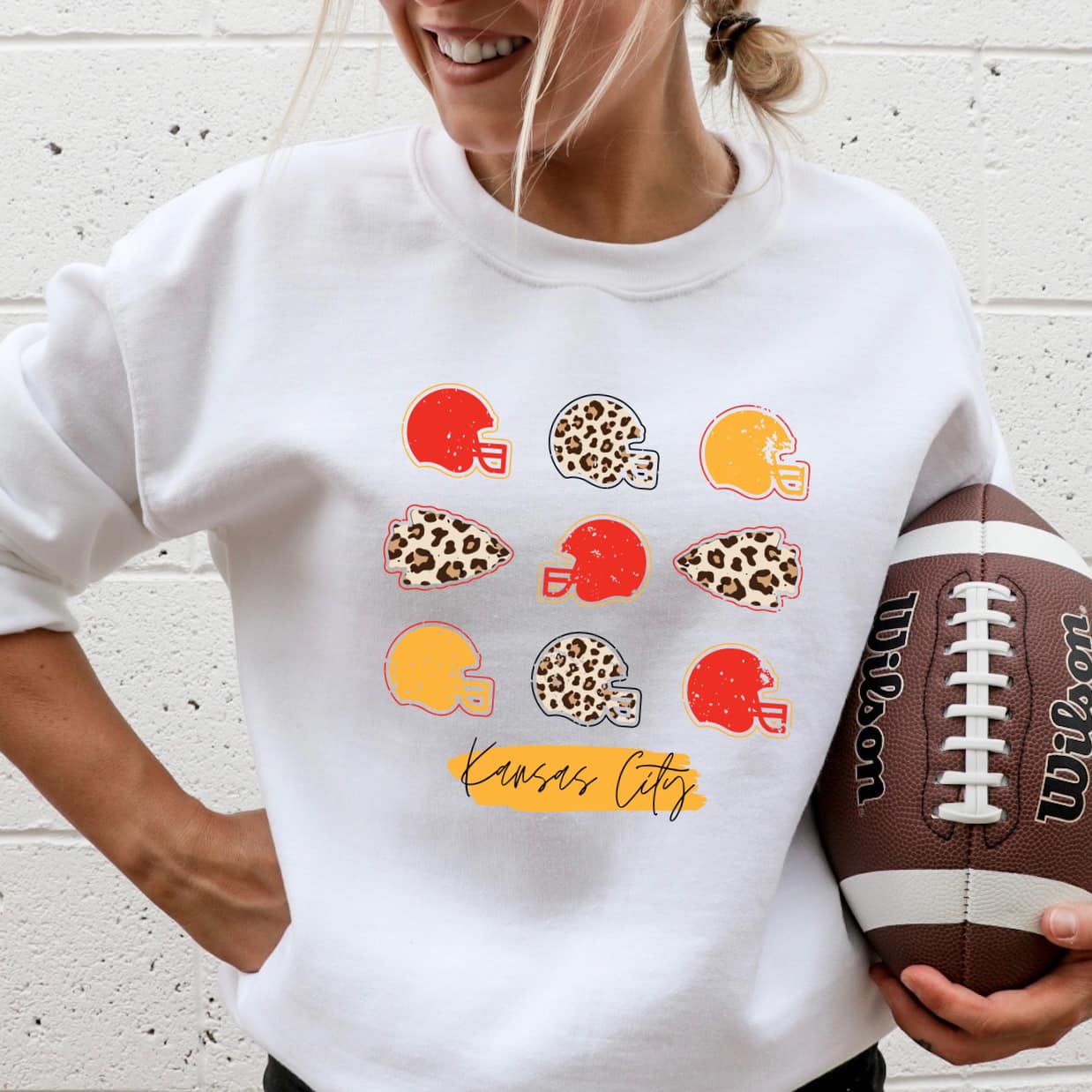 The product photo provided is only a mock up of the design. The design print is colored in red, gold and leopard print. It has pictures of 9 football (3 rows of 3) helmets that are of those colors and two arrowheads in leopard print. Underneath the helmets it says Kansas City. Design is pressed on a white sweatshirt. 