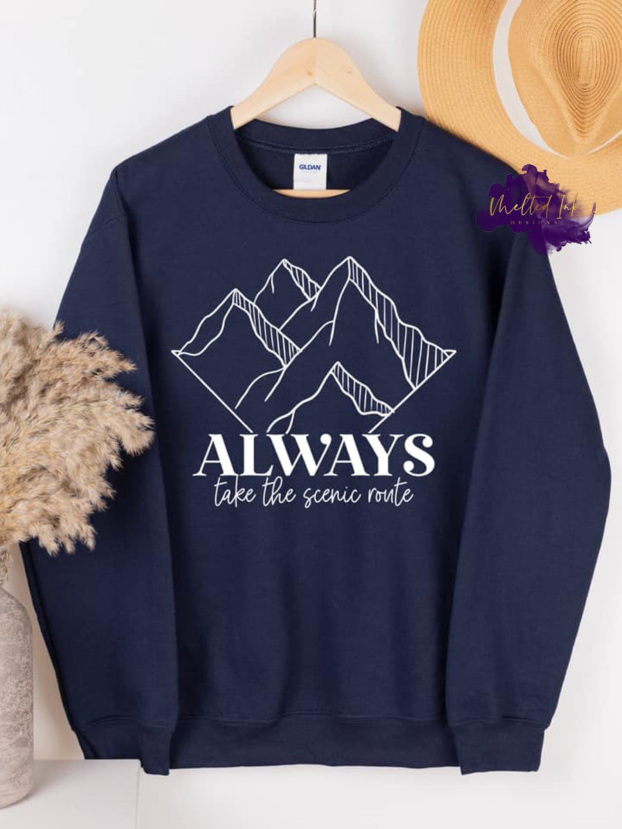 Photo is a mock up of the design. Design print is white and pressed on navy blue sweatshirt. Design says always take the scenic route and has a picture of mountains. 