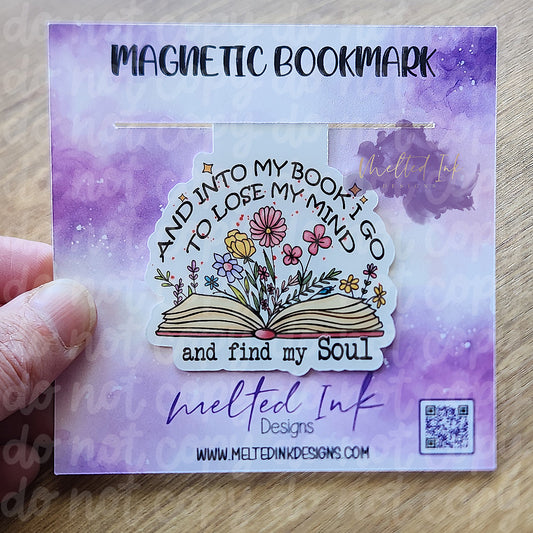 This magnetic bookmark beautifully captures the sentiment "And into my book I go to lose my mind and find my soul." The design features an open book with vibrant flowers seemingly blooming from its pages, symbolizing the transformative power of reading. 