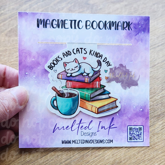 This magnetic bookmark perfectly embodies a cozy reading vibe with the phrase "Books and cats kinda day." It features a stack of books topped with a relaxed cat lounging comfortably. Next to the books, there's a warm cup of coffee, adding to the inviting atmosphere. 