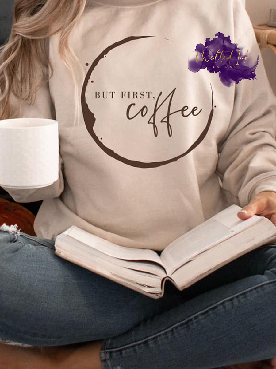 Photo is a mock up of the design. Design print is brown and is pressed on a sand colored sweatshirt. Design says but first coffee and has a circle around the words that appears as a coffee stain. 