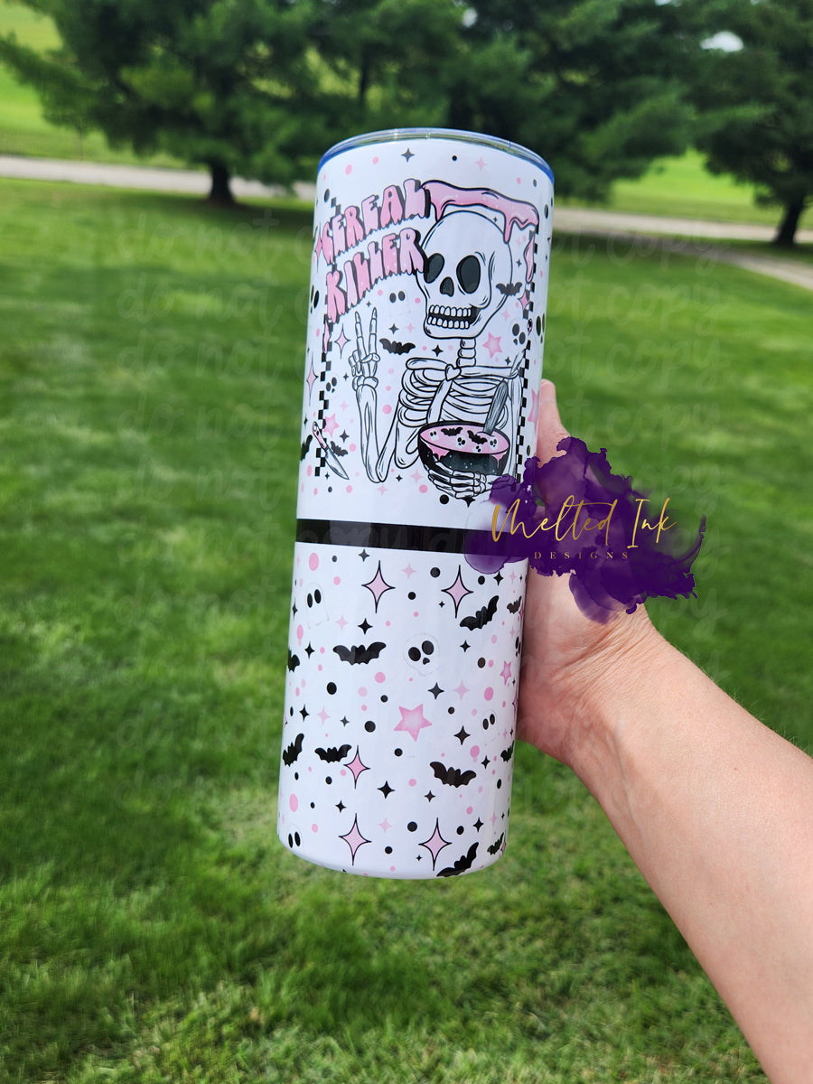 Photo features a 20oz tumbler with a skeleton holding up two fingers giving the peace sign and holding a bowl of bat cereal with the other. Cup says cereal killer and features black bats  with pink stars as well as black and pink polka dots and little skeleton faces. 