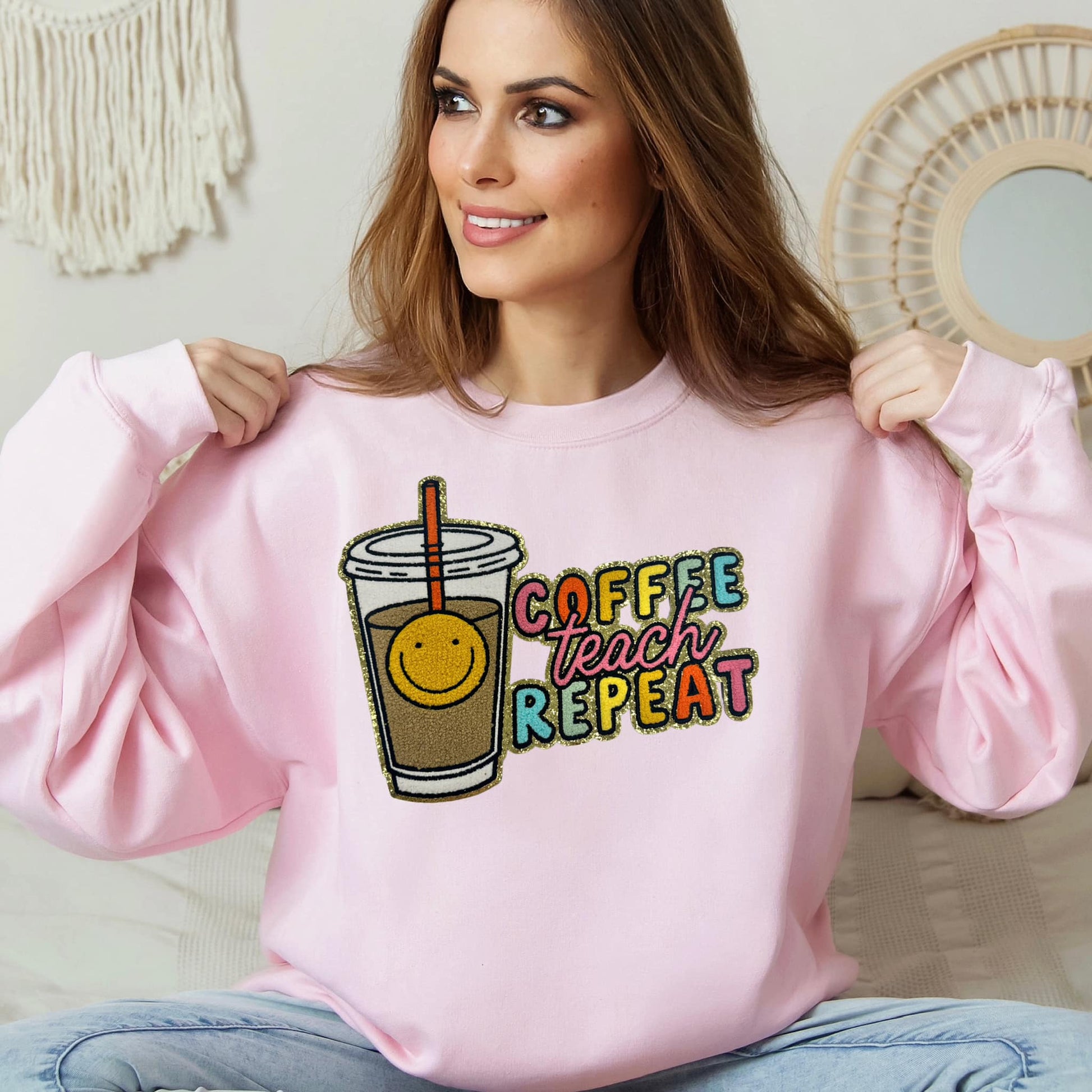 Photo is a mock up of the design. Design is a chenille patch pressed on a pink sweatshirt. Design says coffee teach repeat and has a picture of a drink cup with a straw that has a smiley face. 