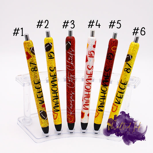 Photo shows 6 different epoxy giltter Chiefs ink pens. 
- #1 is a golden yellow glitter that says Kelce 87 & has a couple hearts & footballs on it. -#2 has yellow glitter & says Mahomes 15 & has a heart & football.-#3 has red glitter & says Kansas City Chiefs & has a yellow heart/football. -#4 is white glitter with Mahomes & 15. Also has several hearts that are yellow & red. 
-#5 is red/yellow ombre glitter & says Mahomes 15 & has yellow/red hearts. - #6 is yellow glitter with Kelce 87 with a heart/football