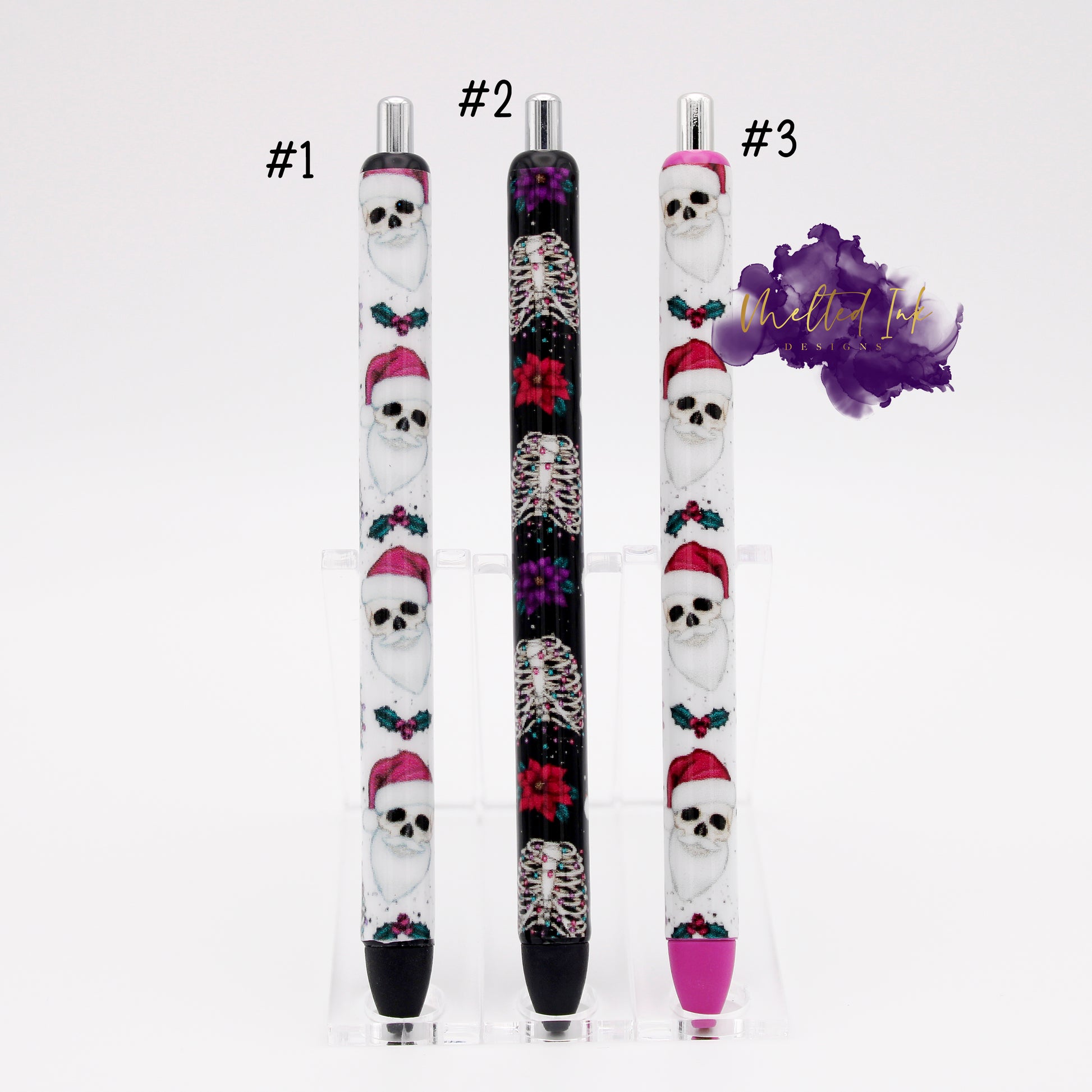 Photo consists of 3 different epoxy pens. #1 has a white background with a skeleton wearing a pink santa hat and has black ink. #2 has a black background with skeleton ribs with christmas lights strung through as well as poinsettas on the wrap and comes with black ink, and #3 has the same design as #1 but is on a pink colored ink pen and has pink ink. 