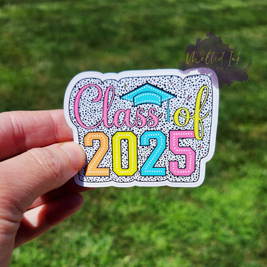 Photo is of a sticker that says class of 2025 and has a black polka dot outline around it. Above the s's in Class is a graduation hat. 