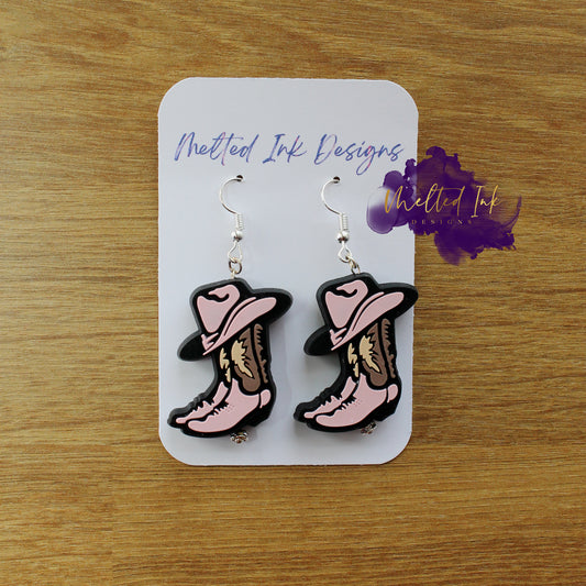 Photo is a picture of a pair cowgirl boots earrings that are pink and brown.