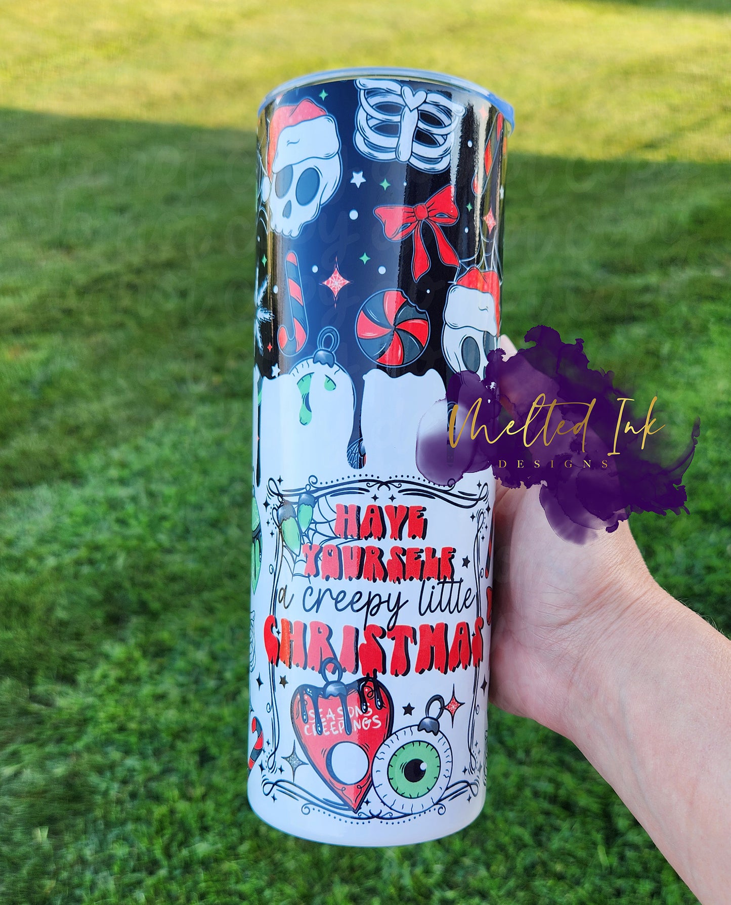 The photo features a festive 20oz tumbler that playfully declares "Have Yourself a Creepy Little Christmas." The design includes a fun skeleton skull wearing a Santa hat, which adds a quirky twist to the holiday theme. Complementing the skull are red bows, red and black candies, and a creepy eye ornament, creating a whimsical yet slightly spooky vibe