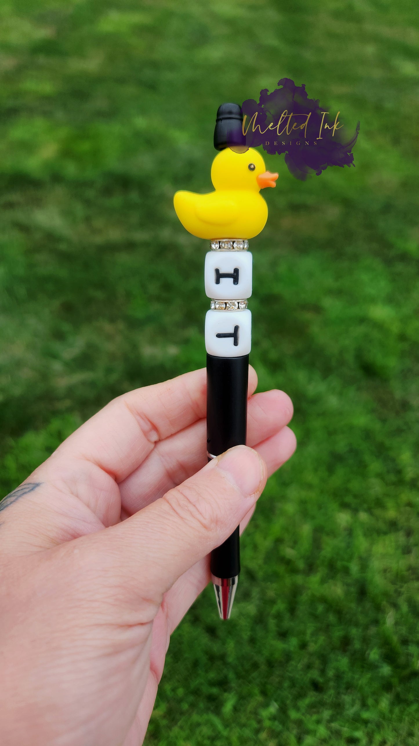 Photo is beaded black ink pen that showcases a yellow duck focal bead. Underneath the duck are letter silicone beads that say IT with spacers inbetween. Ink is black.  