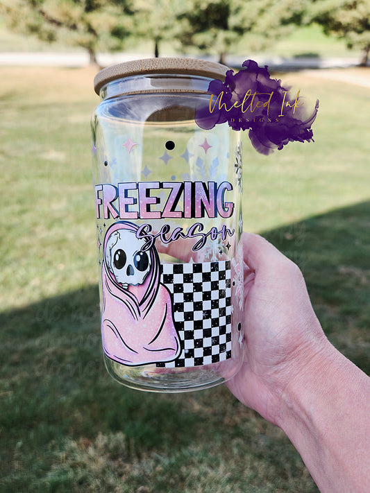 Photo is of a glass can wrap with a skeleton wrapped in a blanket and says freezing season. 