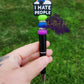 Photo is a black beaded ink pen that has a focal with a rainbow that says I hate people. It is accented with a lime green, blue and purple silicone spacer bead and also has rhinestone spacers. Ink is black. 