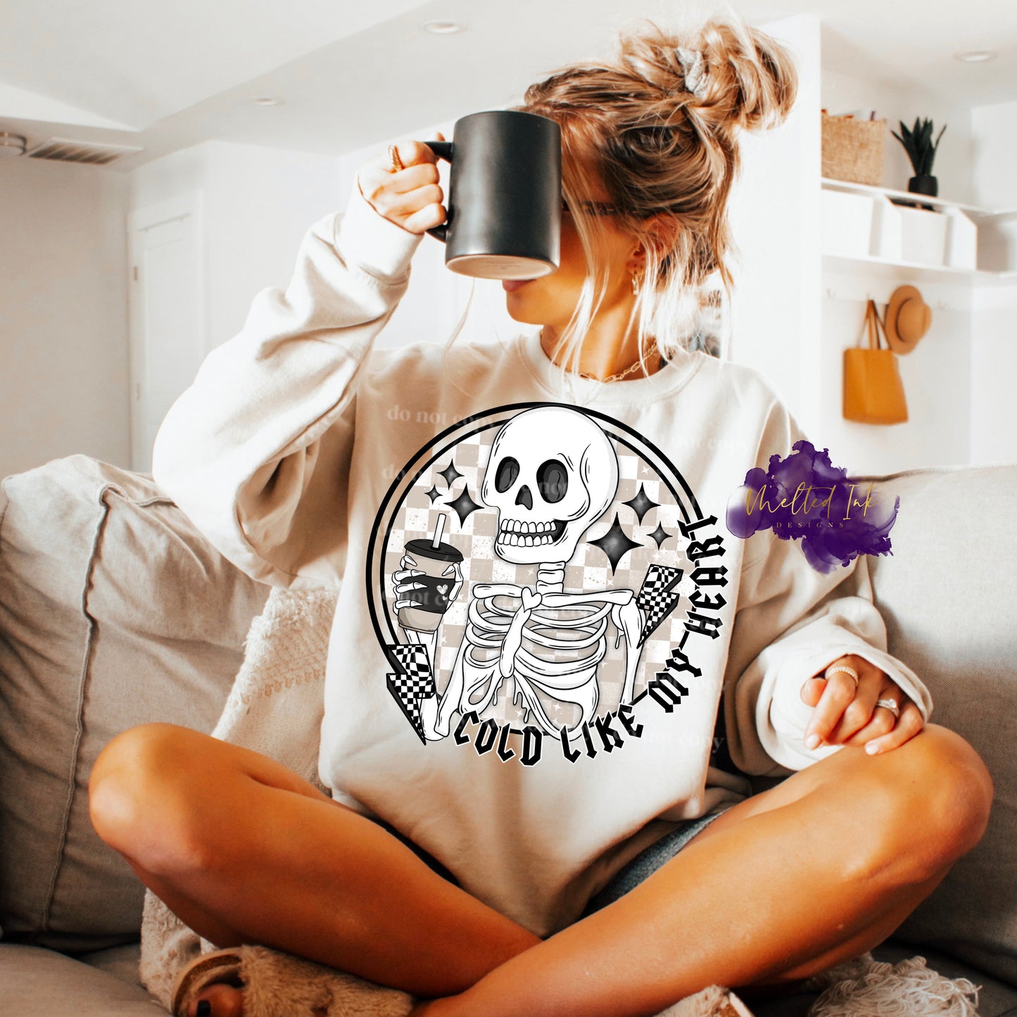 Photo is a mock up of the design. Design is a color print and pressed on a sand colored sweatshirt. Design says Cold Like My Heart and has a white skeleton holding a drink cup with a straw. Also has 2 thunder bolts that are black and white checkered. Background behind the skeleton is tan and white checkered. 