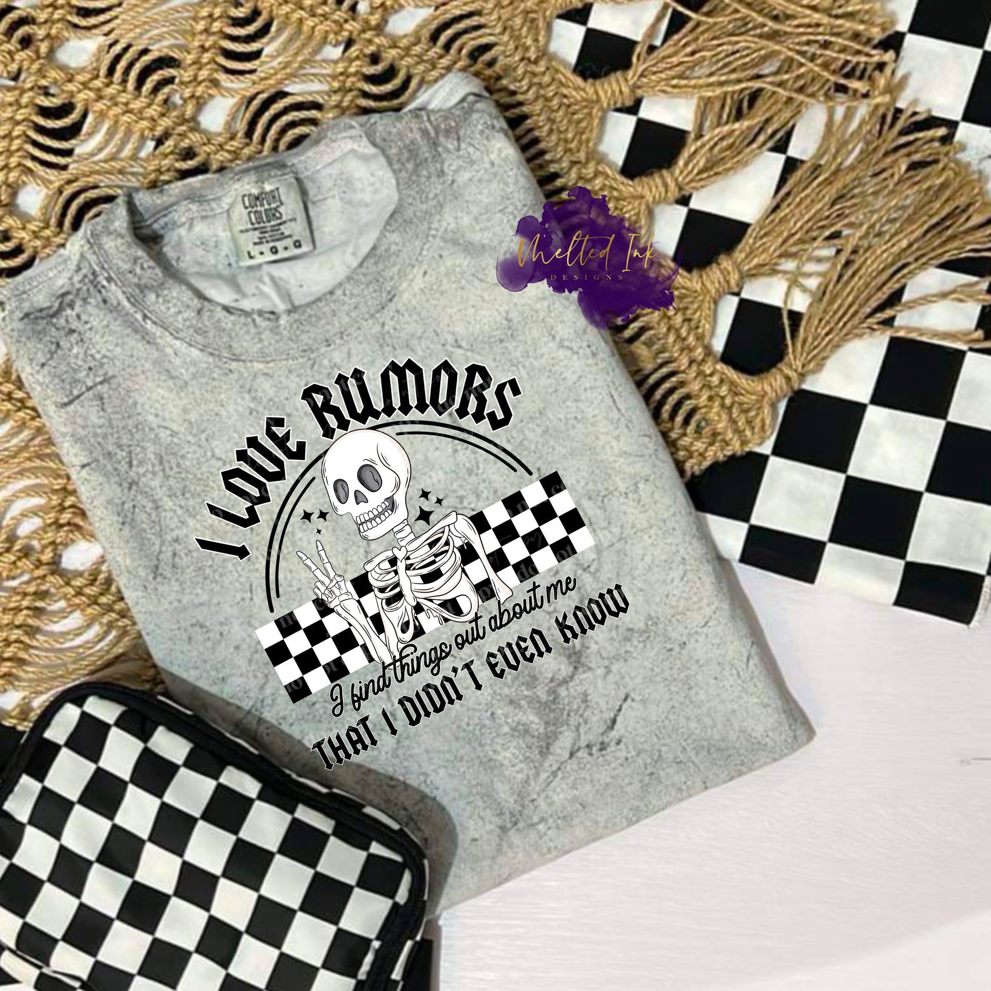 Photo is a mock up of the design. Design is black and white in color and pressed on a smoke blast comfort colors shirt. Design says I love rumors I find things out about me that I didn't even know. Words are black and design has a white skeleton over top a black and white checkered background. 