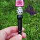 Photo is a black beaded ink pen that has an alcohol bottle focal bead that says I need something you proof and has a cow print bow on it. Accenting the focal bead is a black cow print and a black with white speckled silicone beads and rhinestone spacers. Ink is black. 