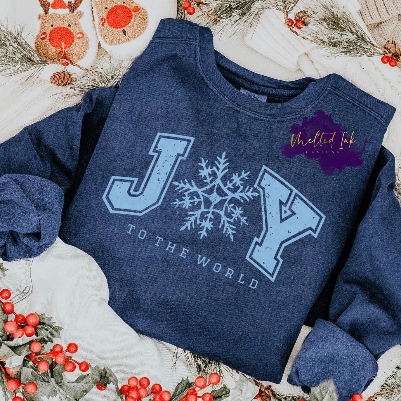 Photo of design is a mock up and is on a blue sweatshirt. Design says Joy the the world in a light blue color. A snowflake is in place of the O in Joy. 