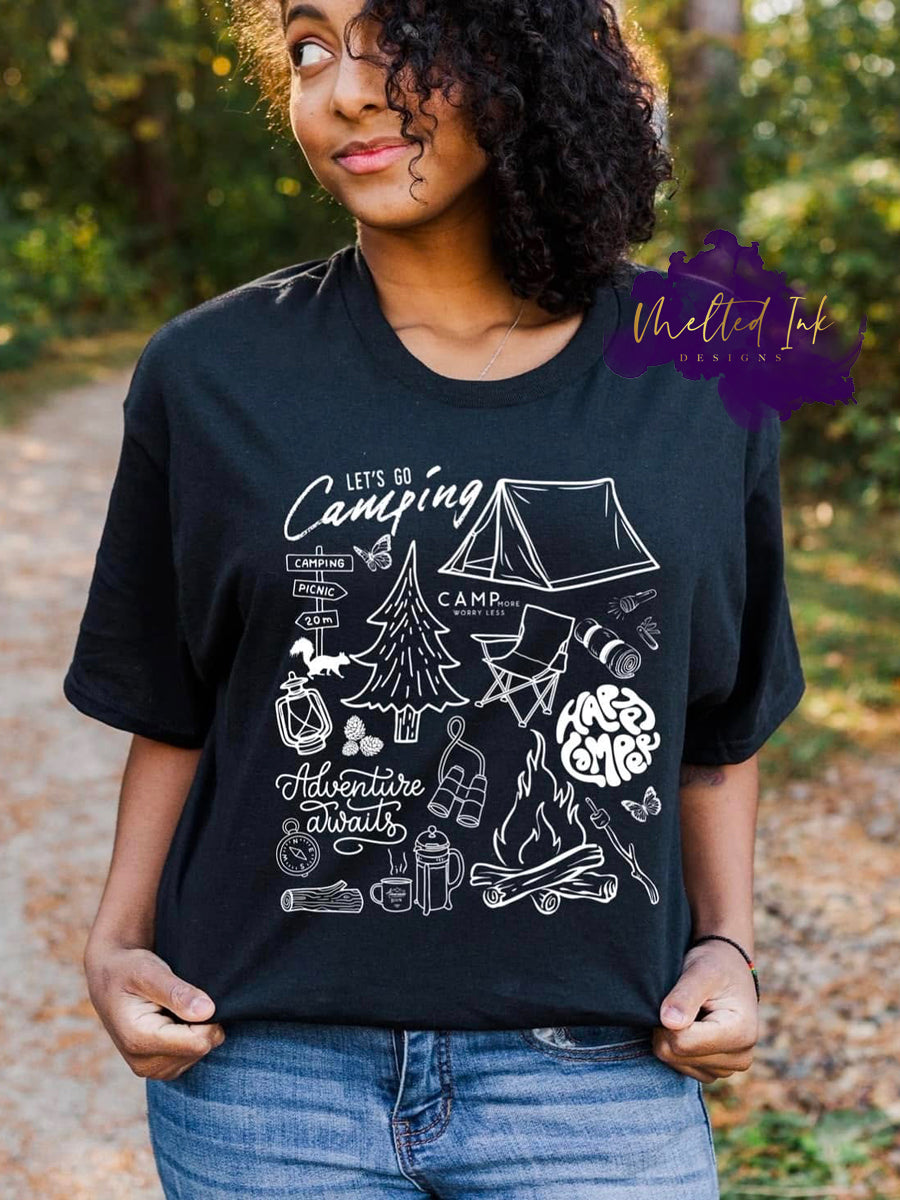 Shirt design with a white outline camping design featuring a tent, lantern, compass, trees, campfire, and text reading “Let’s Go Camping” and “Adventure Awaits.” A nature and adventure themed graphic perfect for shirts, hoodies, and sweatshirts.