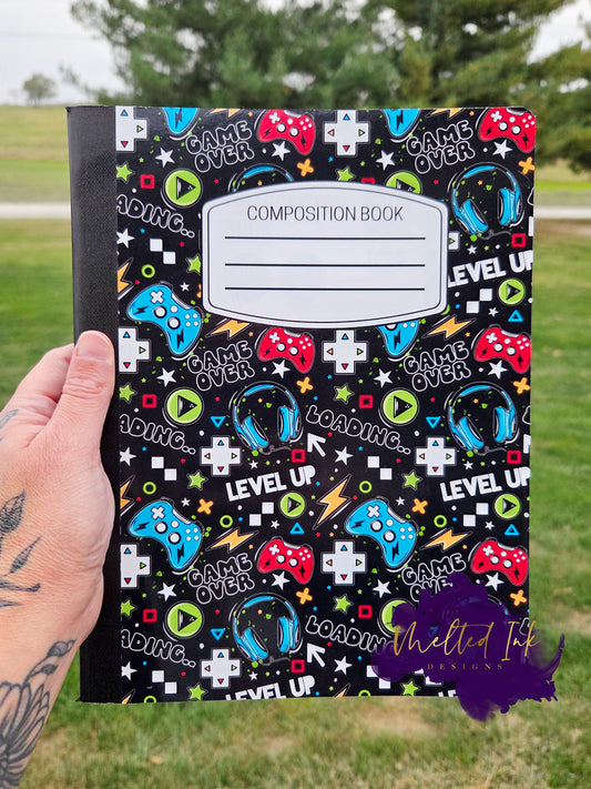 Gaming notebook with colorful controllers, headsets, and gamer text on a black background.