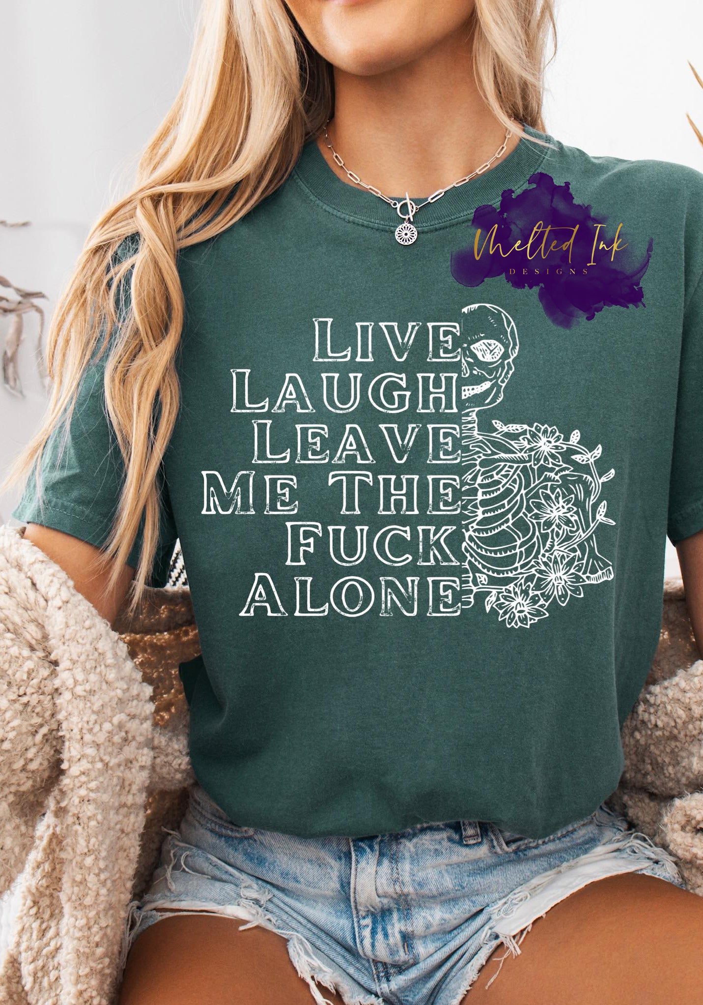 Image shows bold white text reading “Live Laugh Leave Me The Fuck Alone” with a skeleton illustration and floral details surrounding the ribcage.