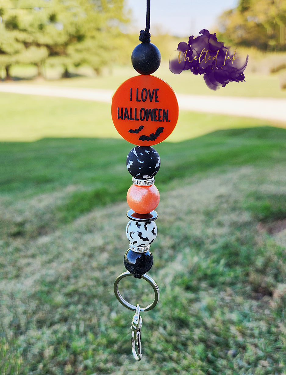 This Halloween lanyard features a fun focal bead that reads "Look, It's Frickin Bats" on one side and "I Love Halloween" on the other. It includes four 15mm silicone beads: a pearl black bead, a pearl orange bead, and two bat-themed beads—one white with black bats and the other black with white bats. The design is enhanced with rhinestone spacers, adding a touch of sparkle, and it comes with a keyring for practicality.