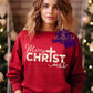 Photo is a mock up of design and is on a red sweatshirt. Design is beige color and says Merry ChrTstmas (The I in Christmas is a cross)